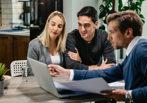 Young couple and real estate agent using laptop while going through housing plan on a meeting.